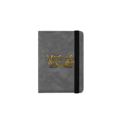 A grey passport holder with a gold We The Way Apparel logo on the front.